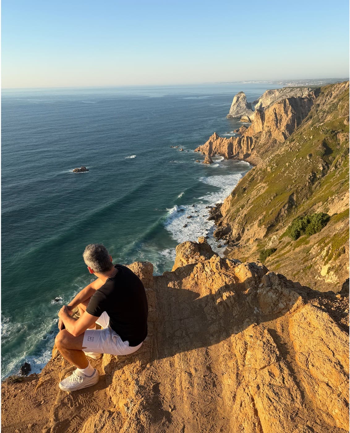 Pedro sitting on a cliff edge above the Atlantic Ocean at Cabo da Roca, Portugal.